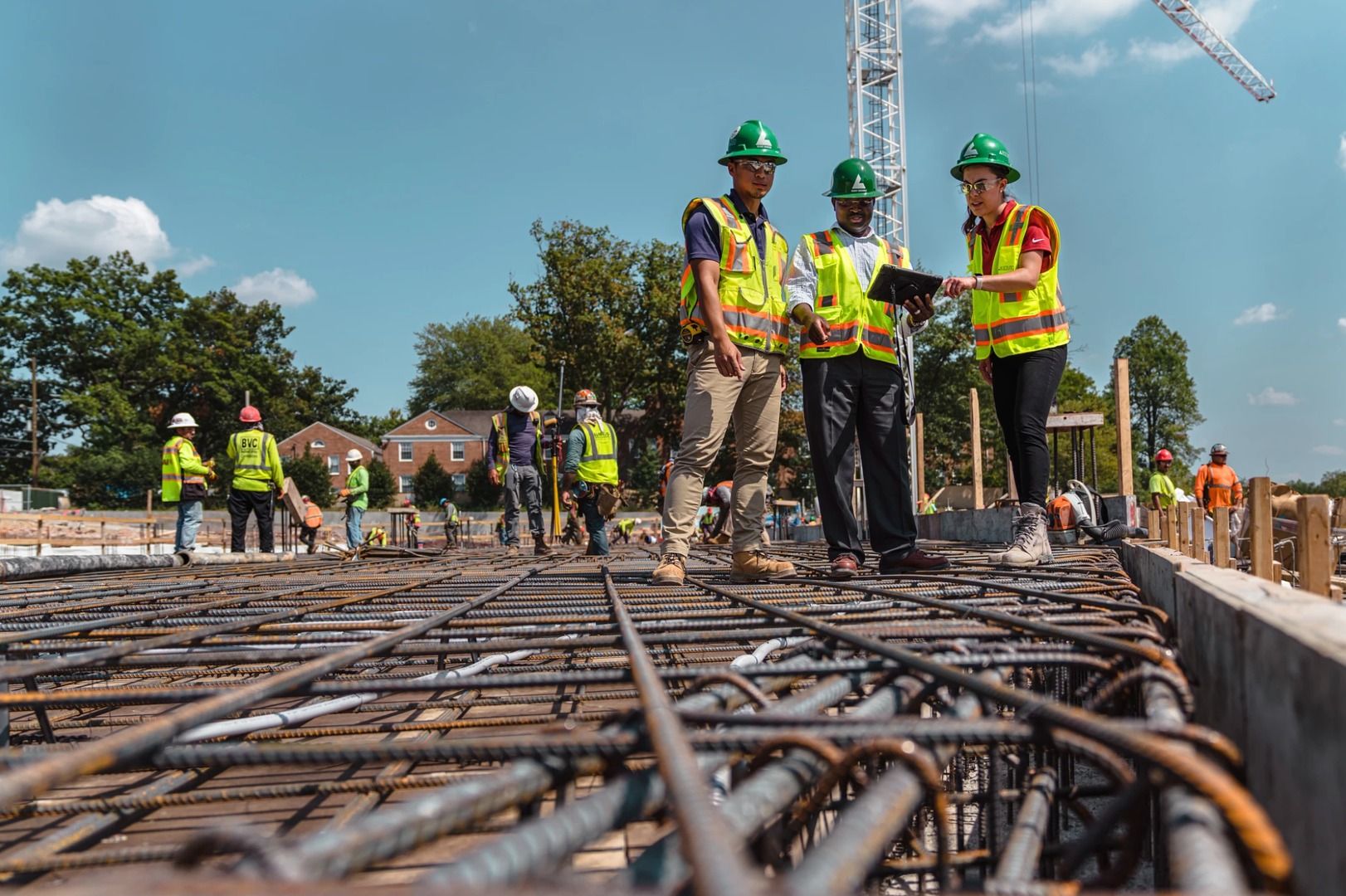 Construction site with workers in safety gear reviewing plans over rebar.