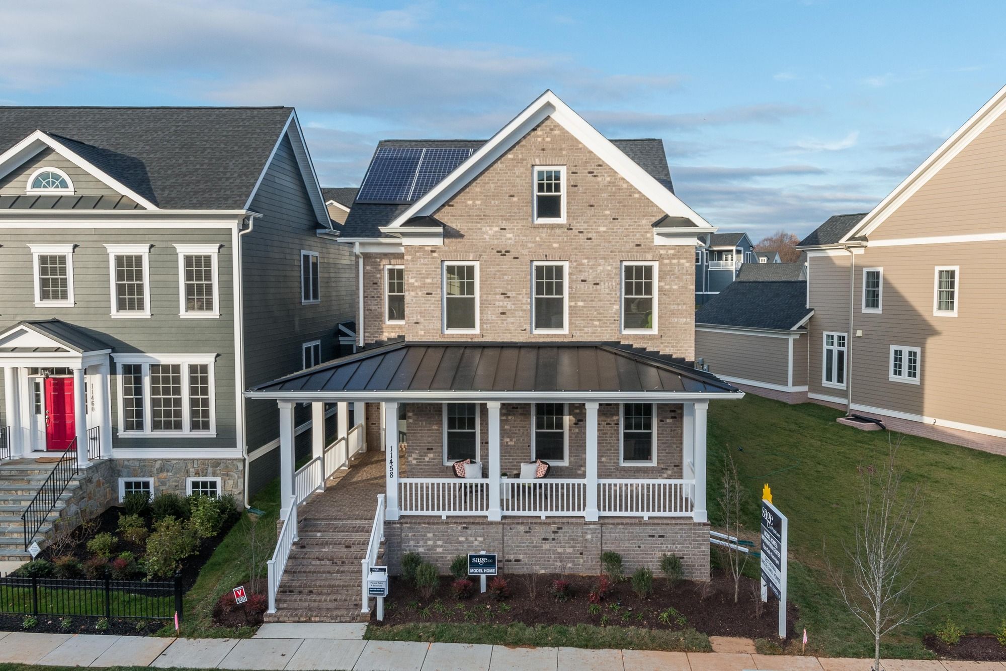 Two-story house with stone facade, porch, and solar panels, surrounded by other homes.
