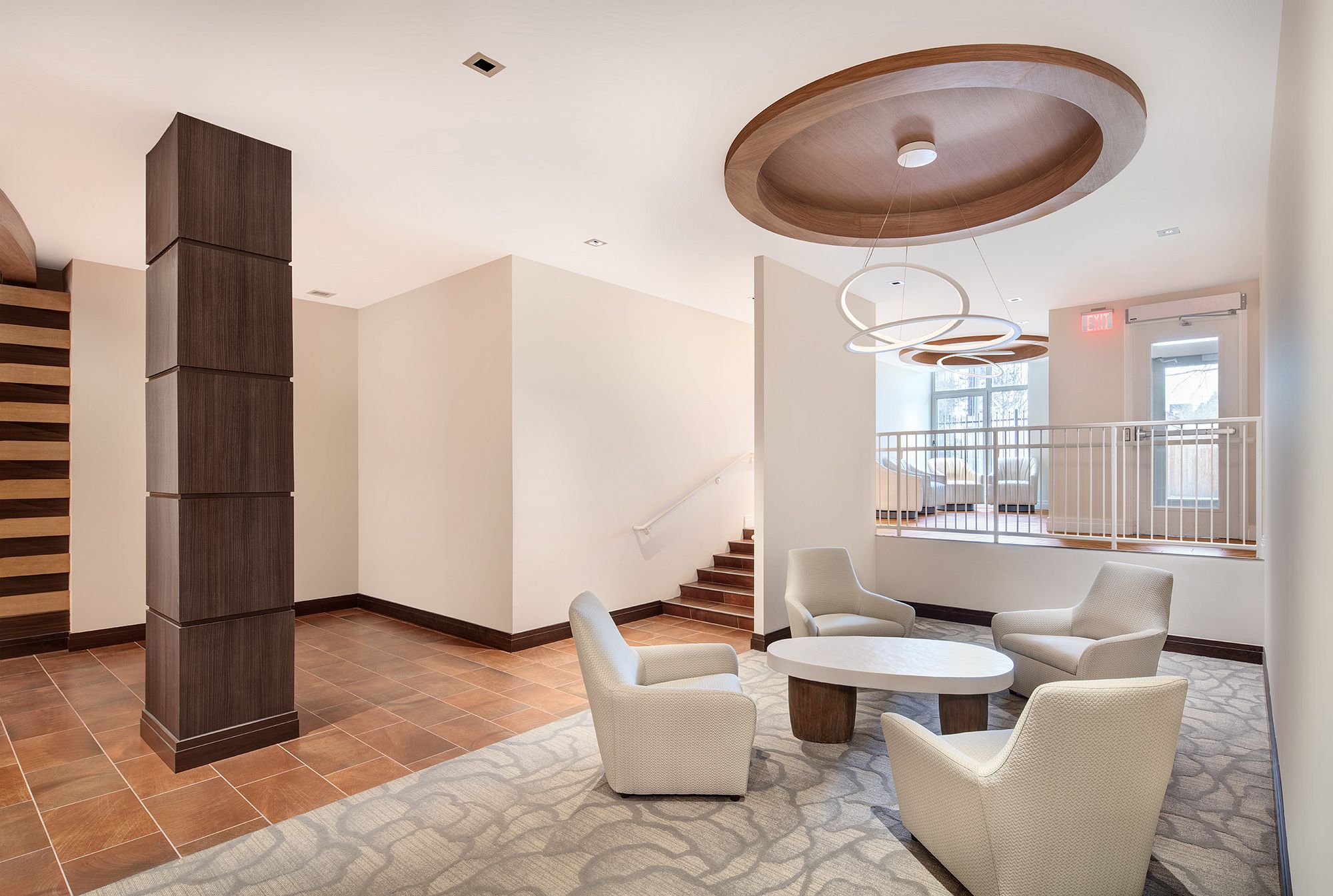 Modern lobby with a round table and four white chairs, featuring a staircase and decorative ceiling.