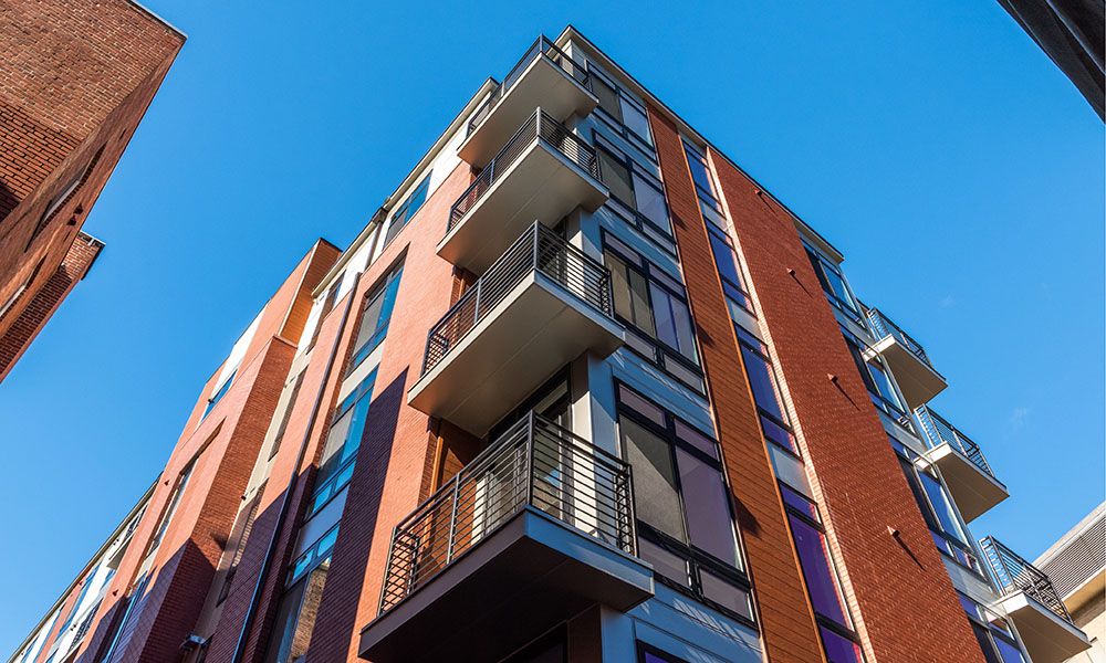 Looking up at a modern red-brick building with balconies against a clear blue sky.