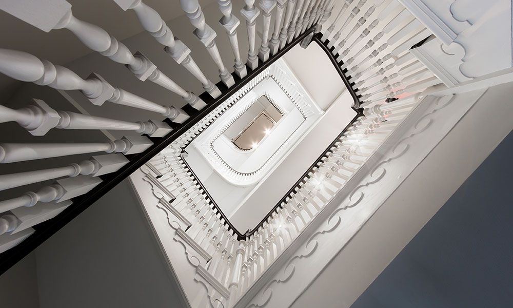 A downward view of a white staircase with railings and light illuminating the space.