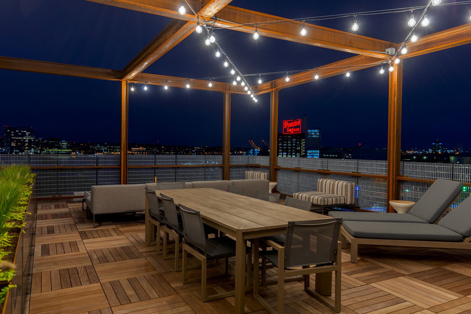 Rooftop terrace with wooden furniture and string lights at night.