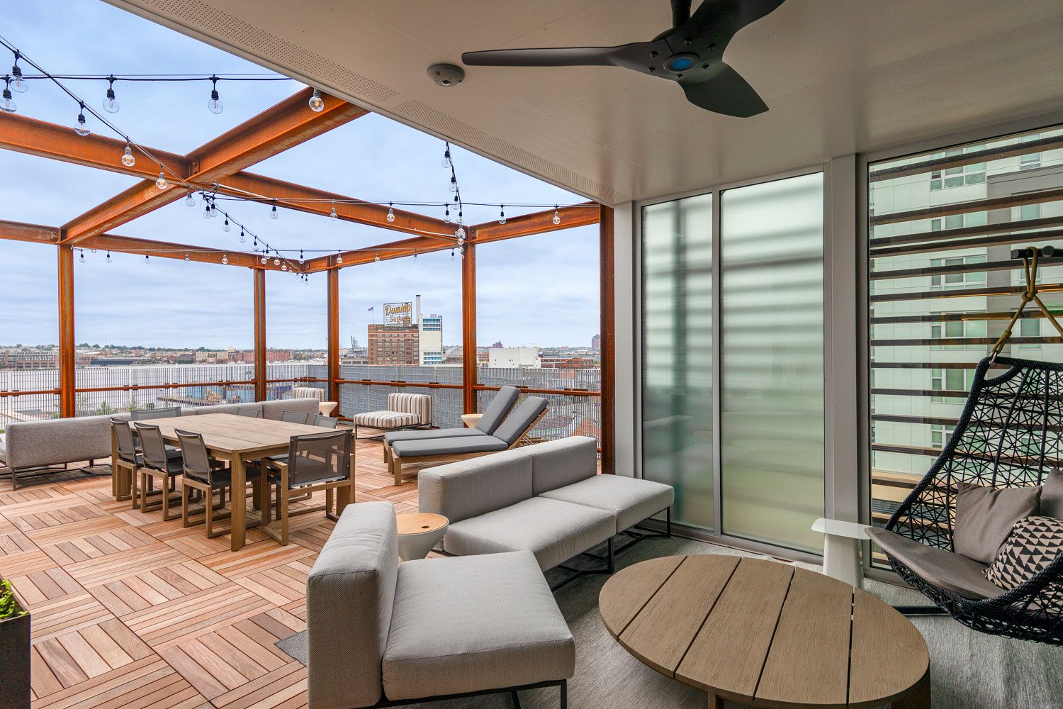Modern outdoor lounge area with seating, dining table, and a hanging chair under a canopy.