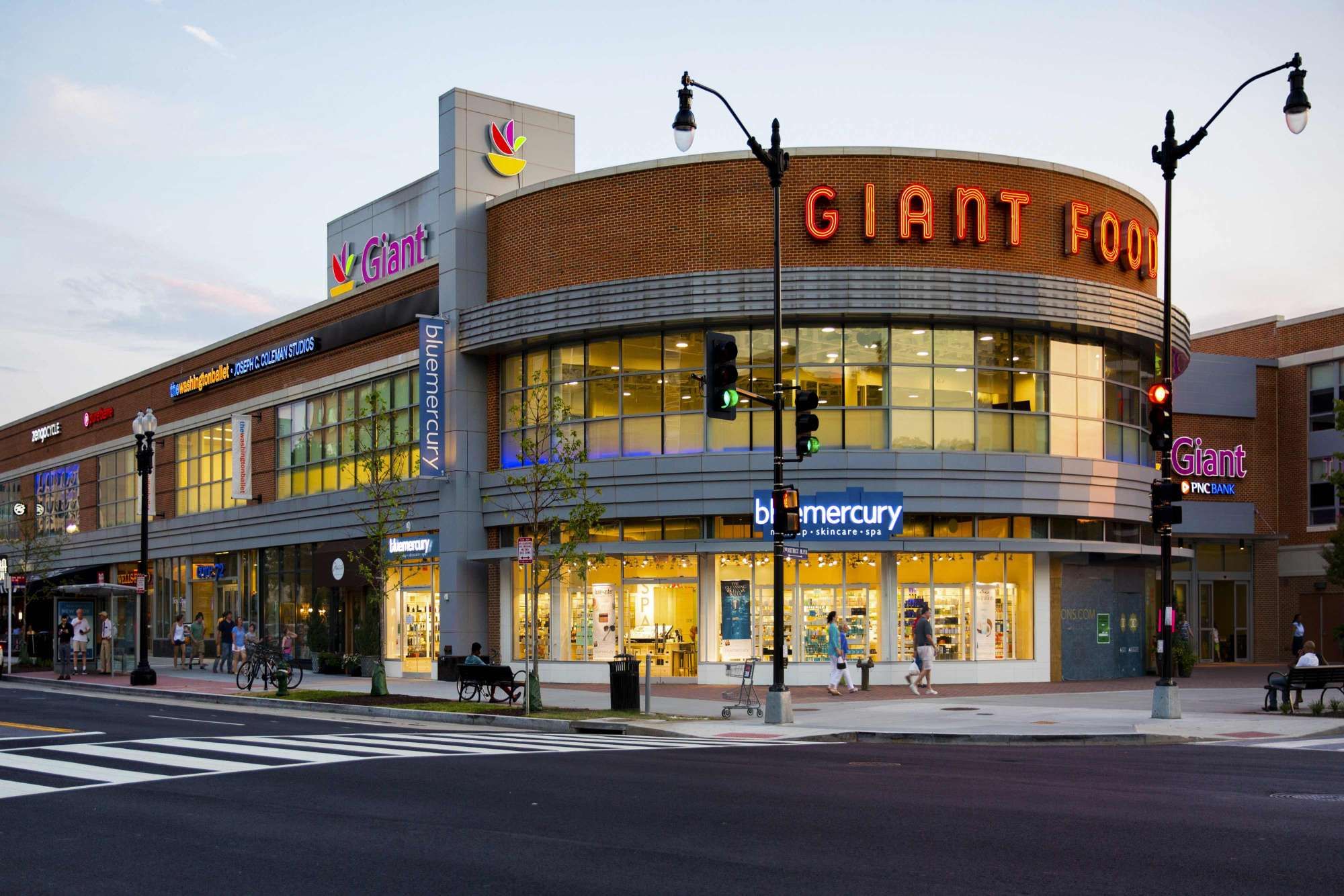 A modern grocery store with large windows and bright signage at dusk.