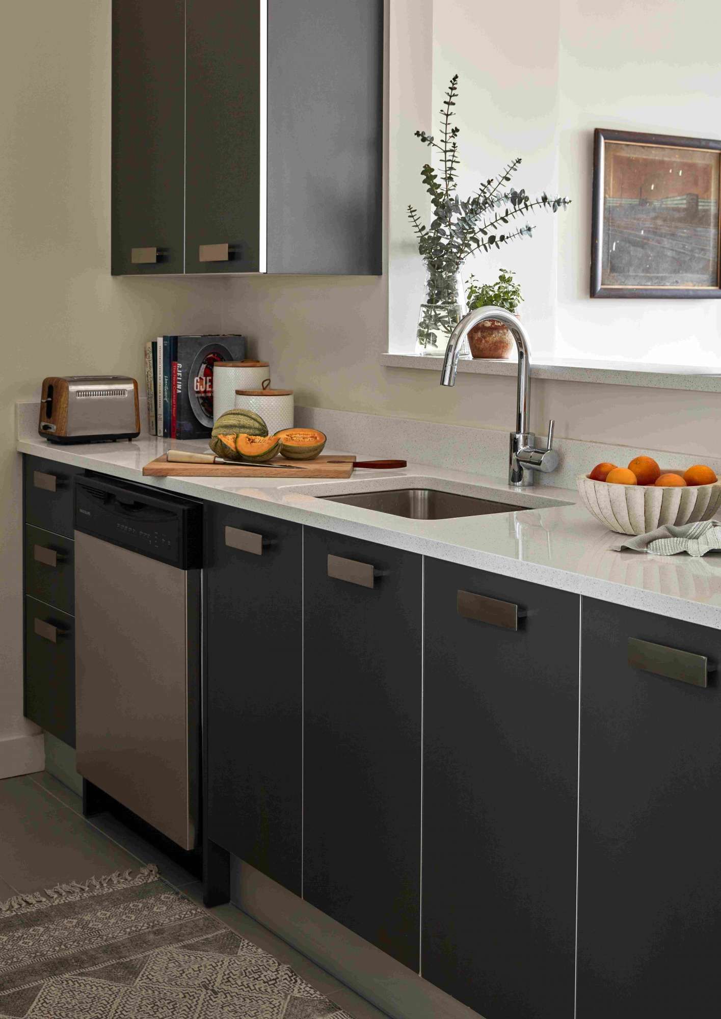Modern kitchen with dark cabinets, sink, and countertop display of fruit and kitchen appliances.