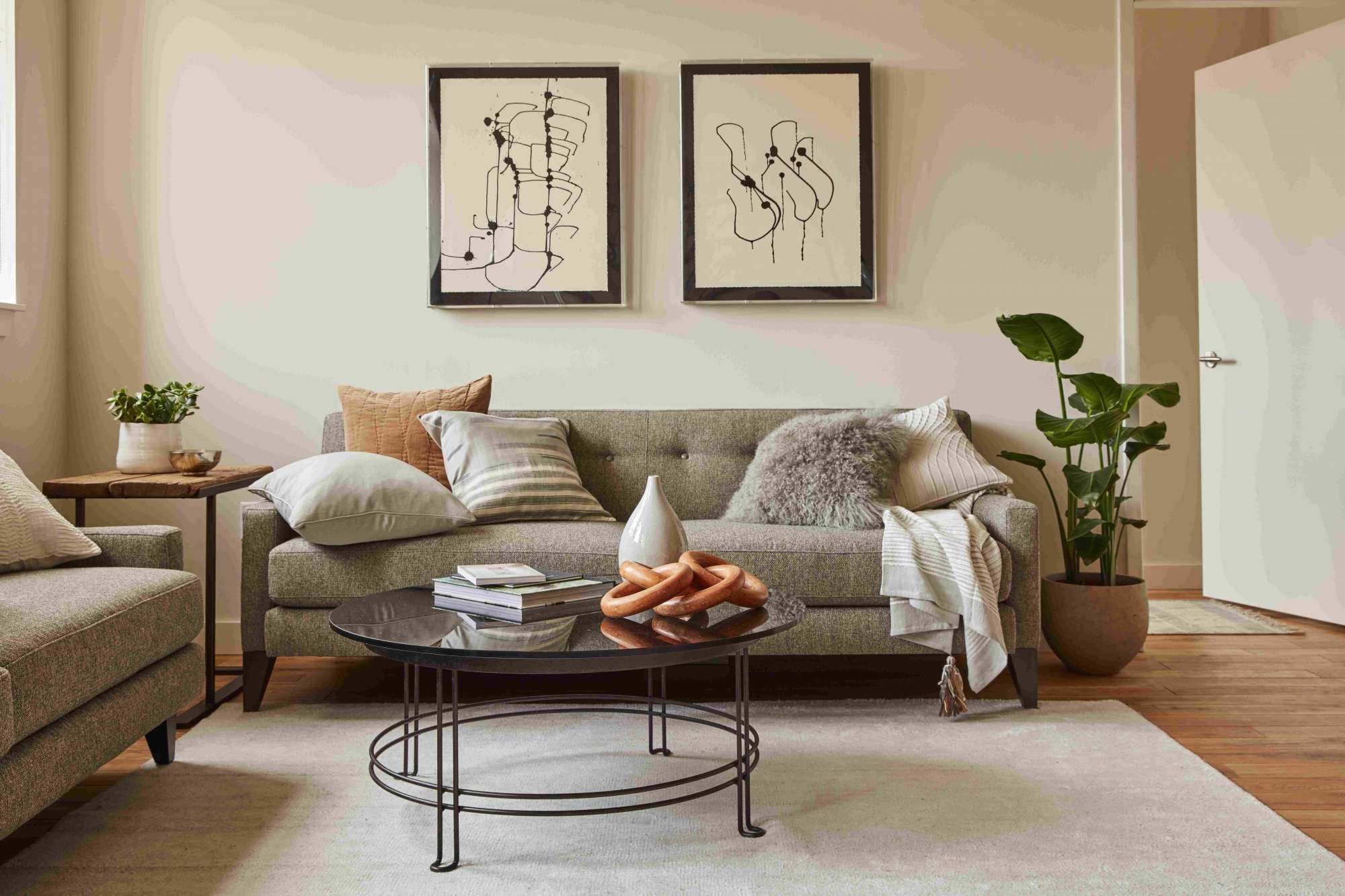 Modern living room with a gray sofa, abstract art, plants, and a round coffee table.