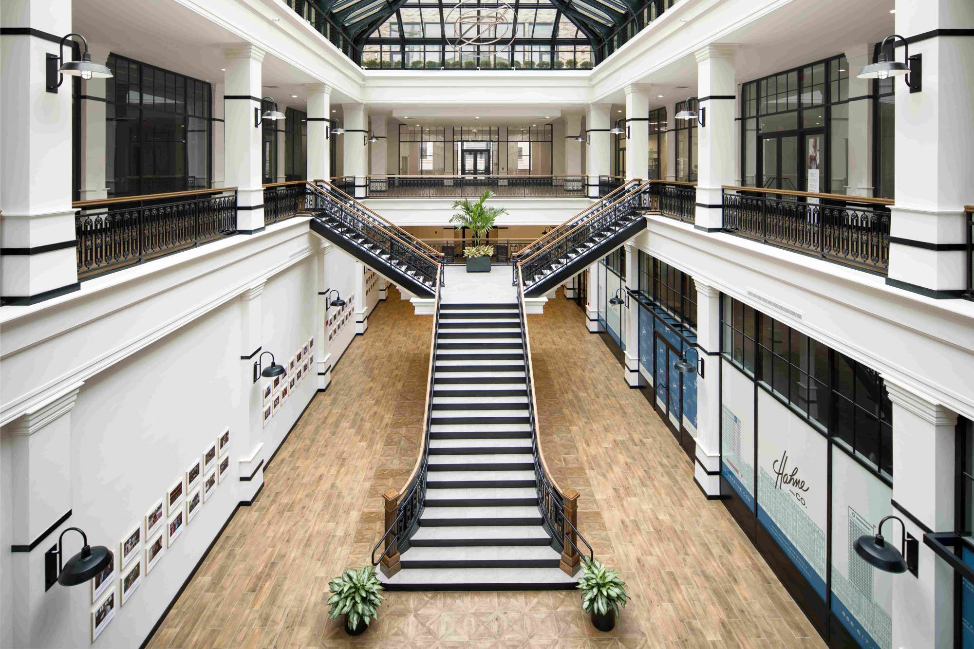 Modern atrium with central staircase and glass ceiling, featuring potted plants.