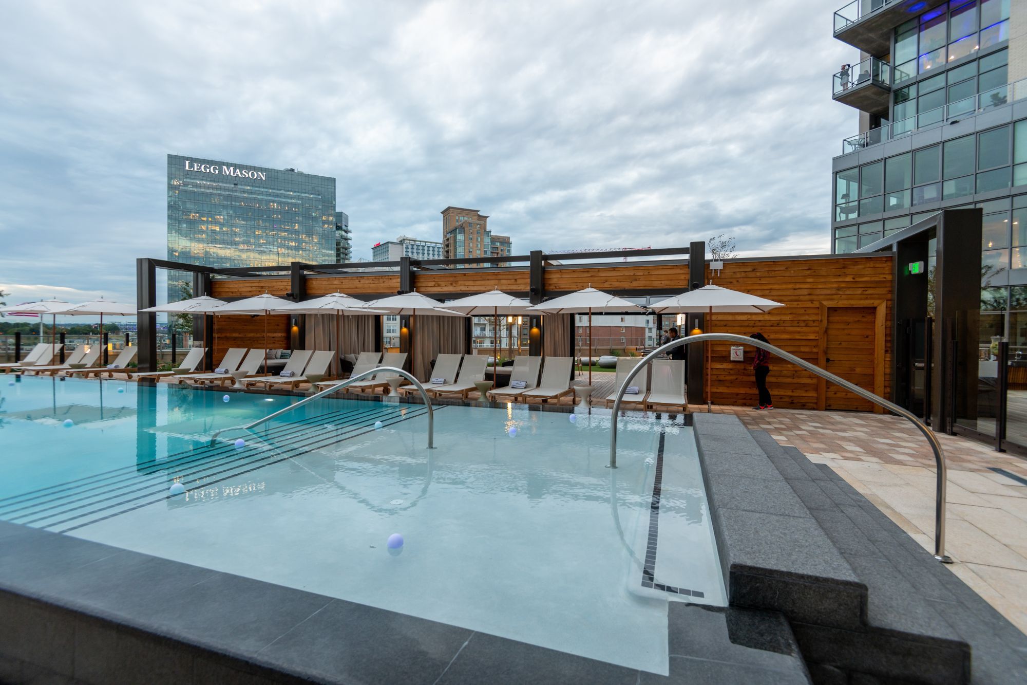 Rooftop pool area with lounge chairs and umbrellas under a cloudy sky.