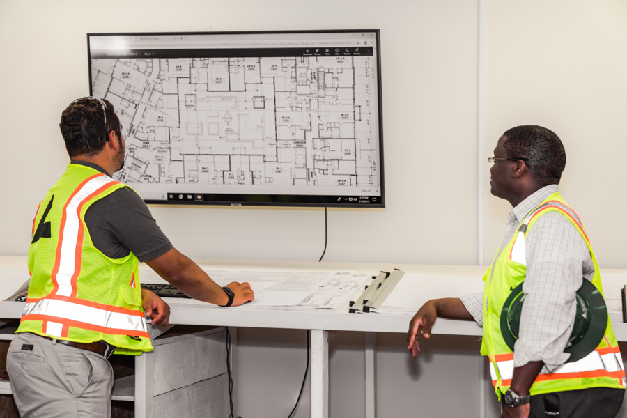 Two construction workers examining building plans on a screen.