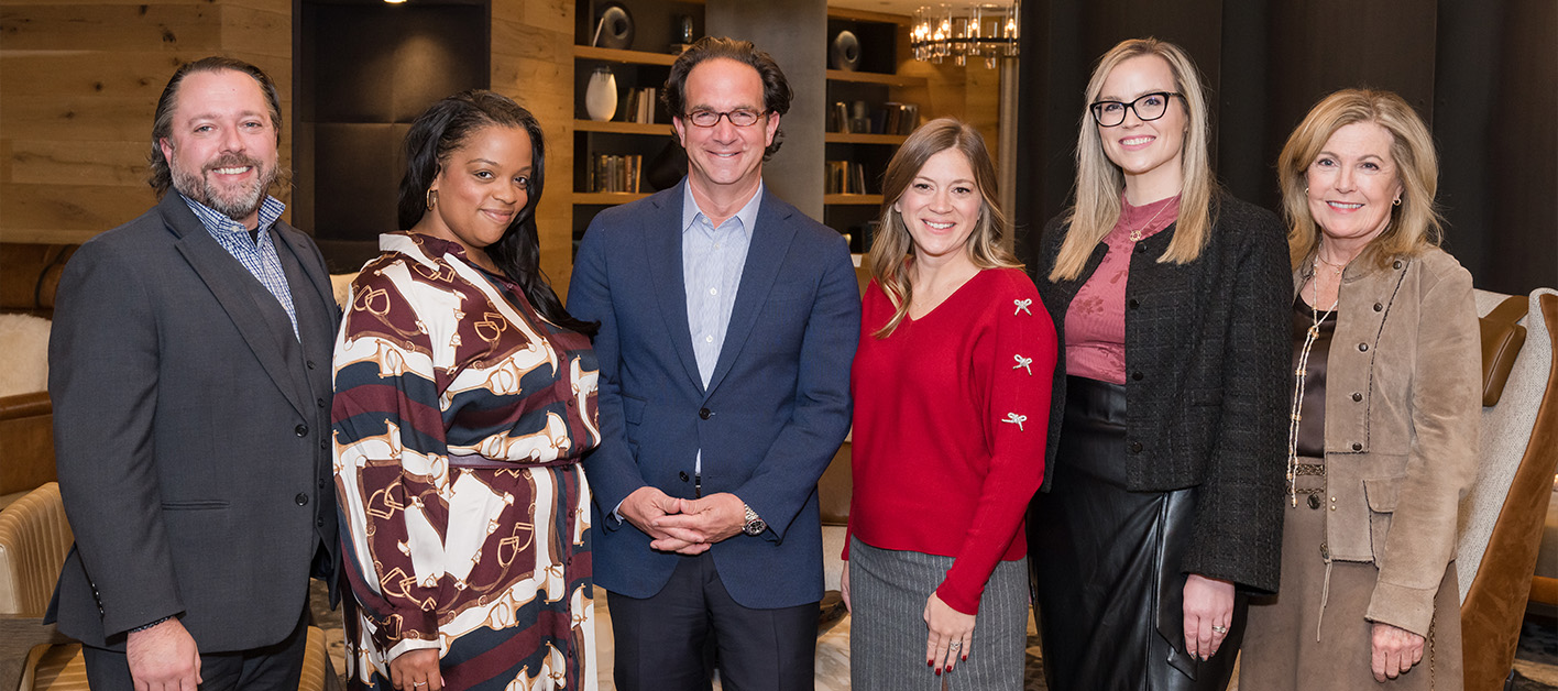 Group of six people standing together in a stylish indoor setting.