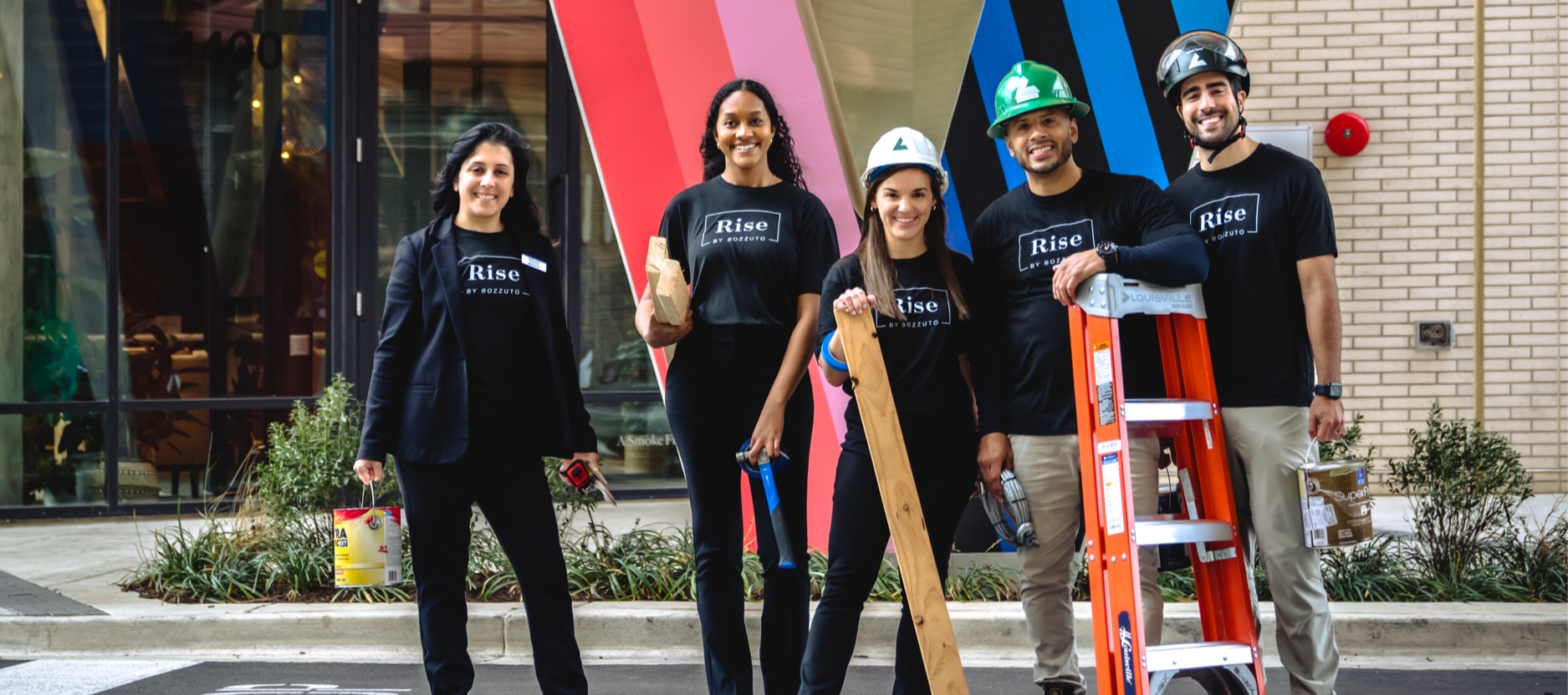 Group of five people in black shirts holding tools and standing in front of a colorful wall.
