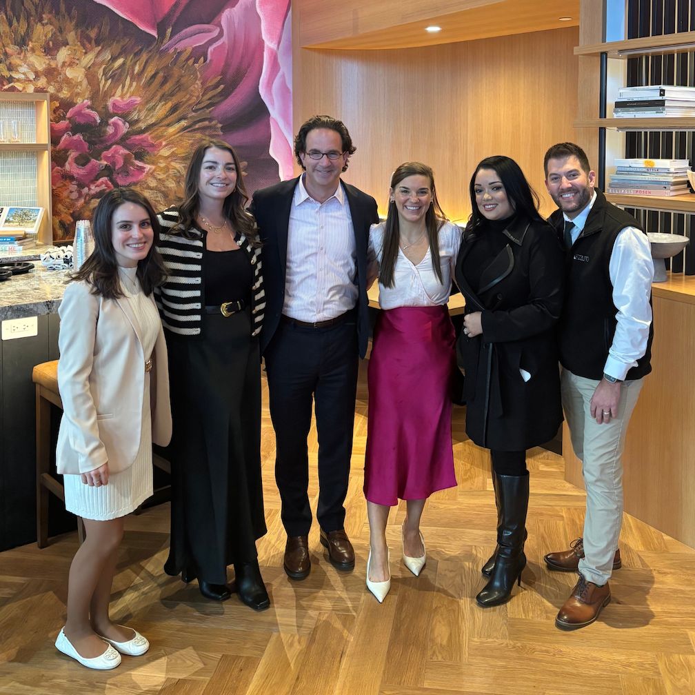 Group of six people posing together in a stylish indoor setting.