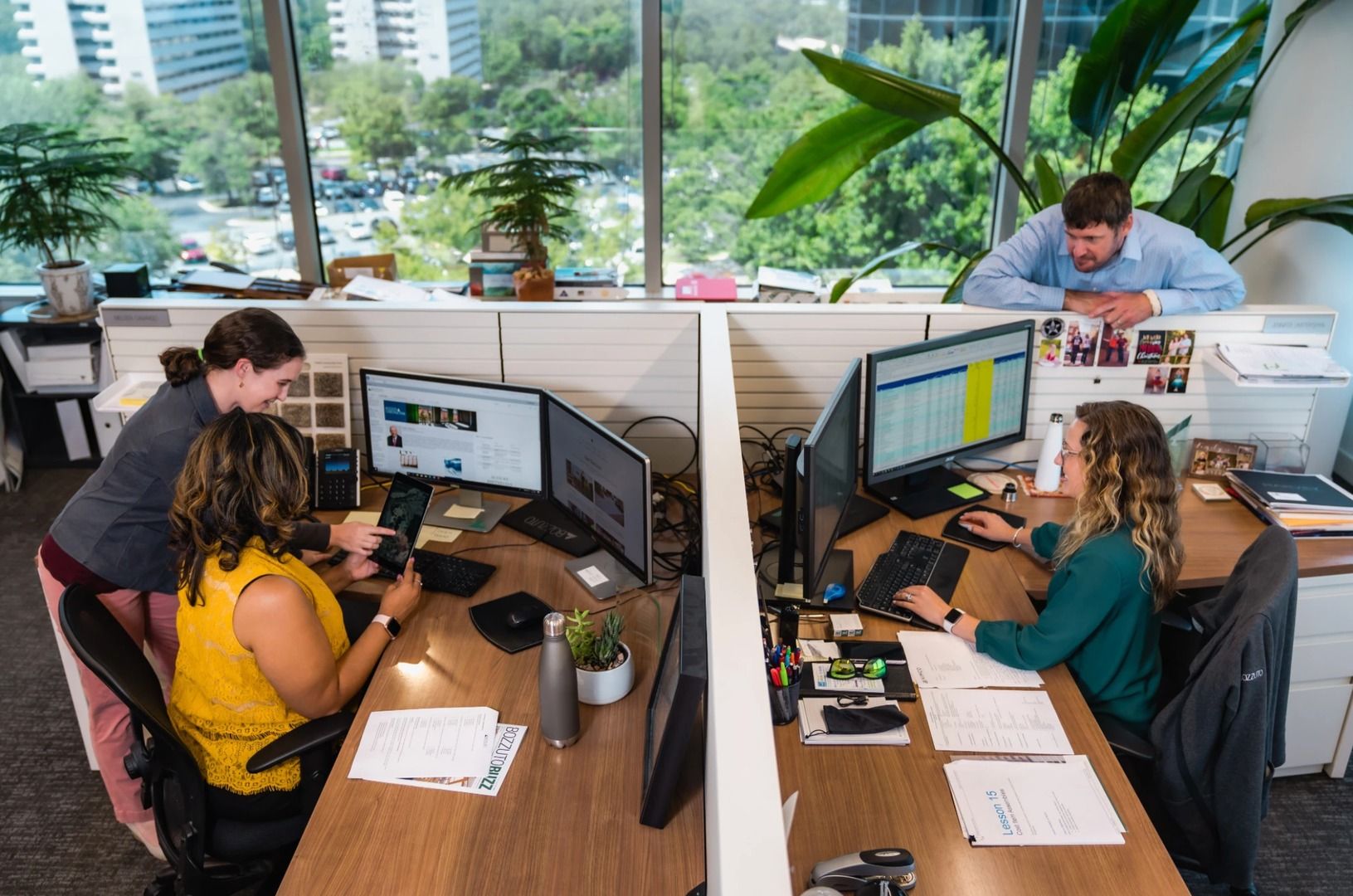 Three coworkers working at desks in a bright office with large windows.