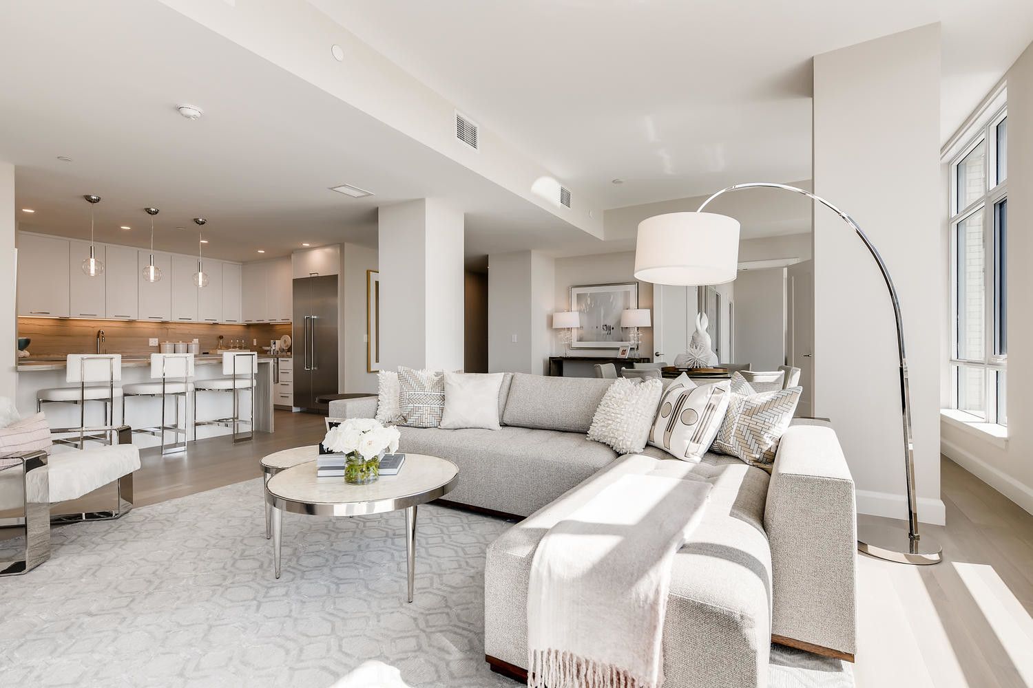 Modern living room with light colors, a sectional sofa, and an open kitchen area.
