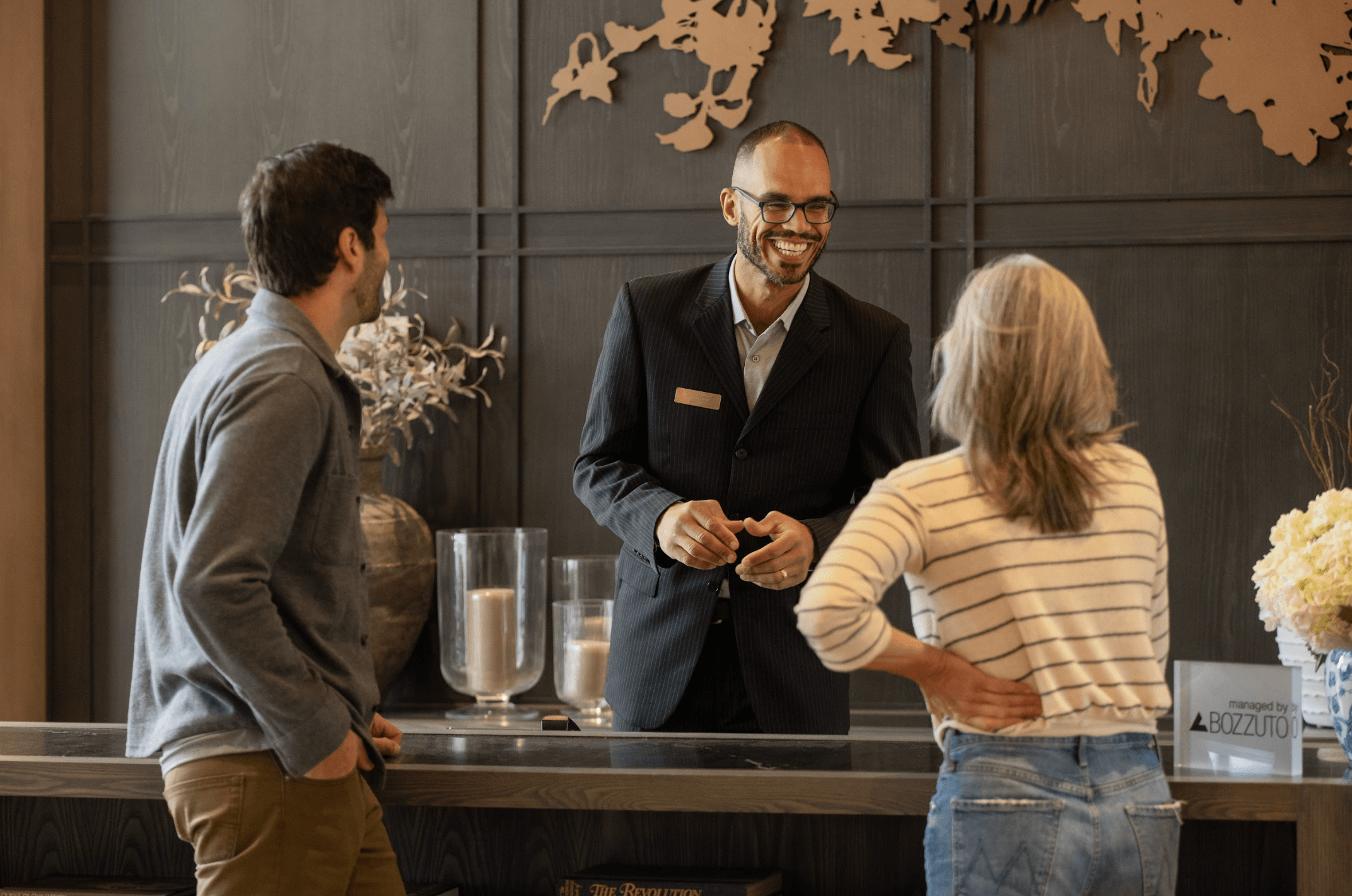 A friendly receptionist assists two guests at a hotel front desk.