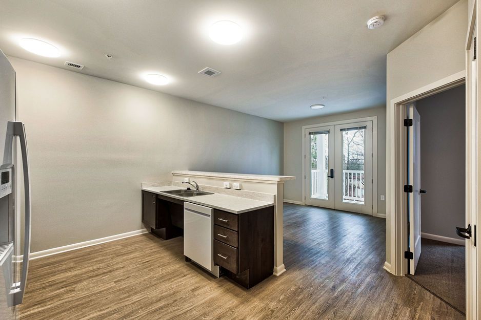 Modern kitchen with stainless steel appliances and wooden floors, leading to an outdoor area.