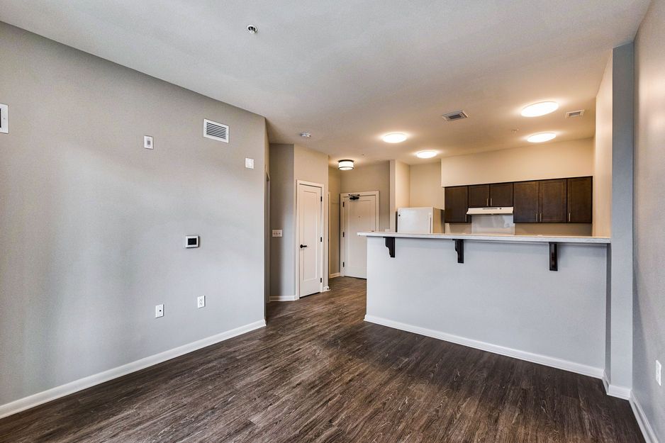 Modern, empty apartment interior with open kitchen and hardwood floors.