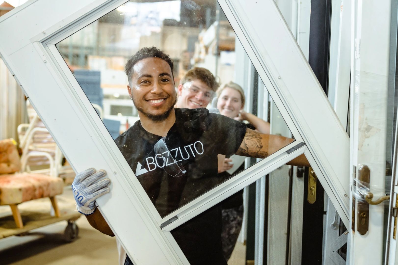 A man holding a large window frame with two people smiling in the background.