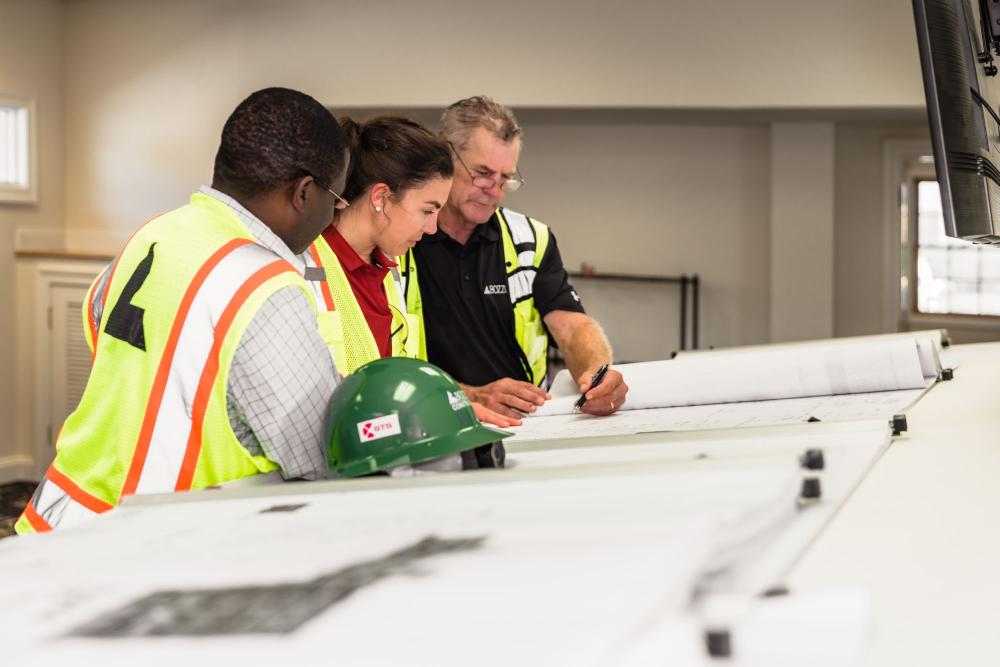 Three construction workers reviewing plans at a worksite.