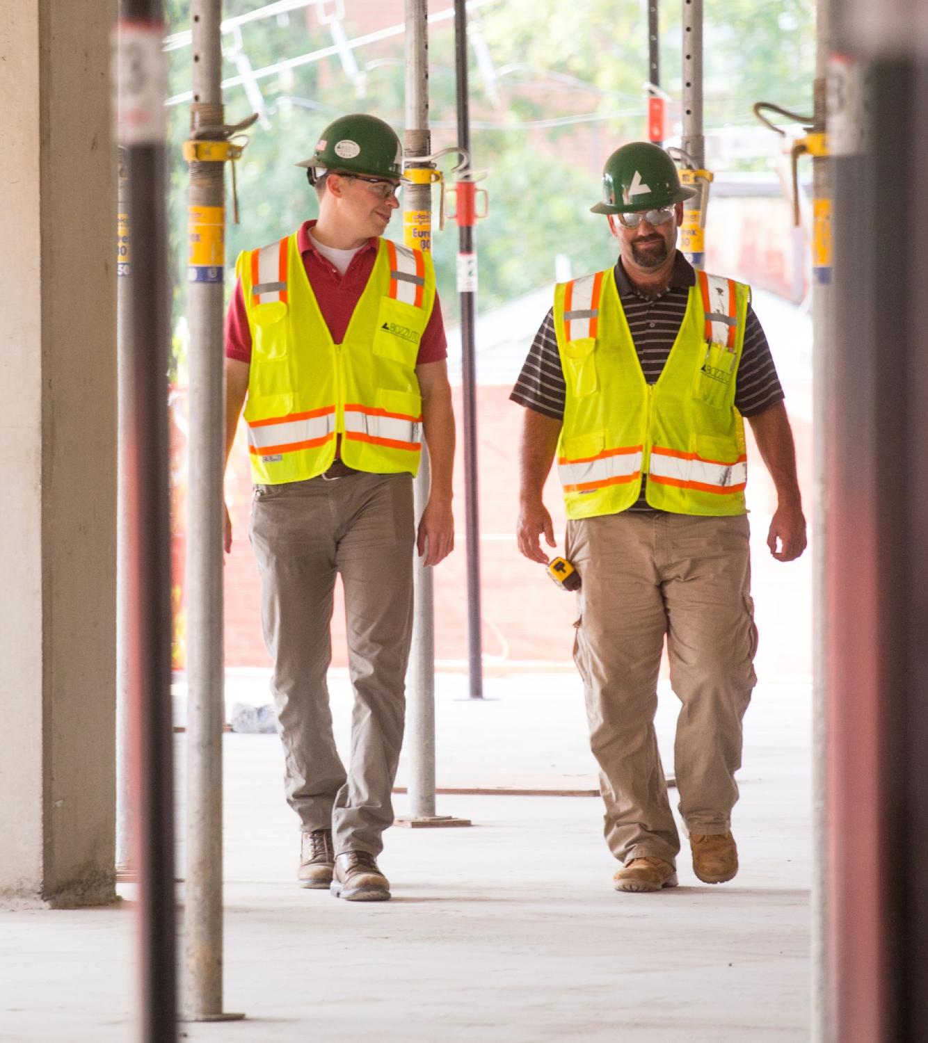 Two construction workers in safety gear walking through a site.