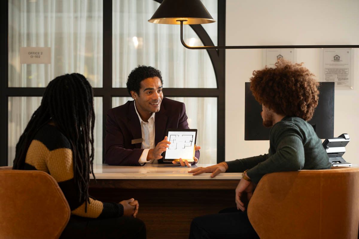 A man shows a tablet to two people at a modern service desk.