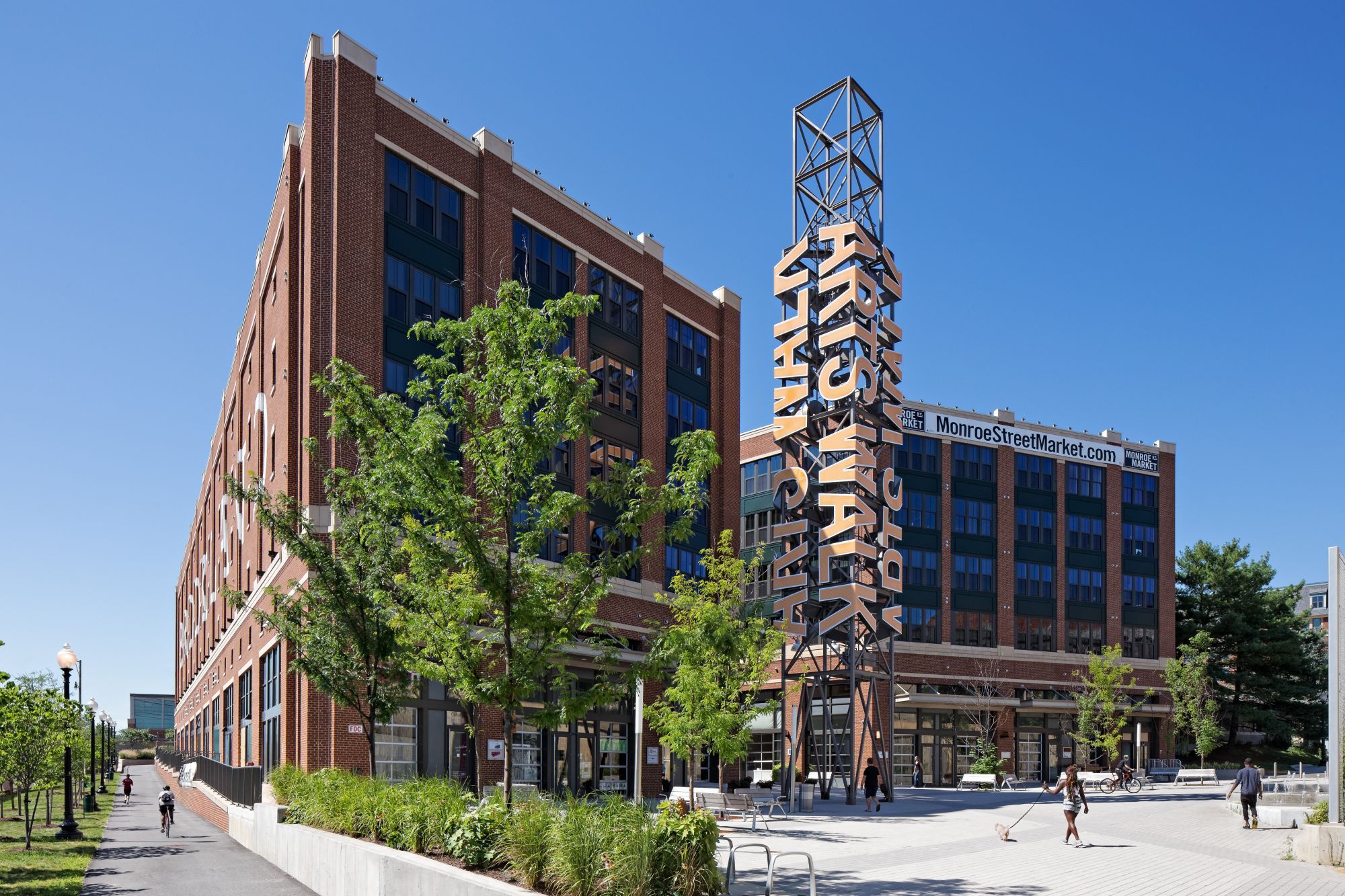 Modern brick building with large windows and a decorative tower, surrounded by greenery.