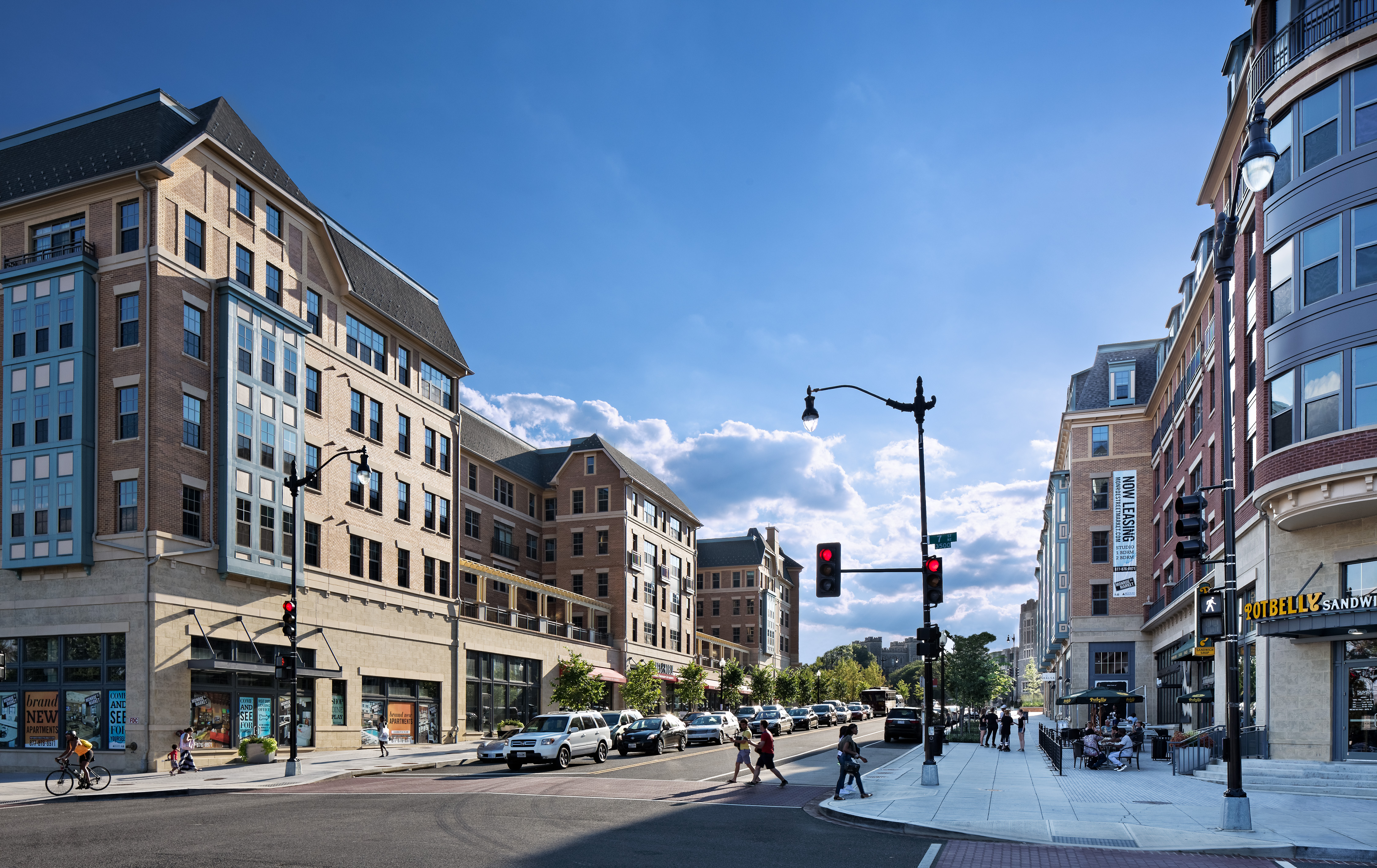 Modern city street with buildings, people walking, and traffic lights.