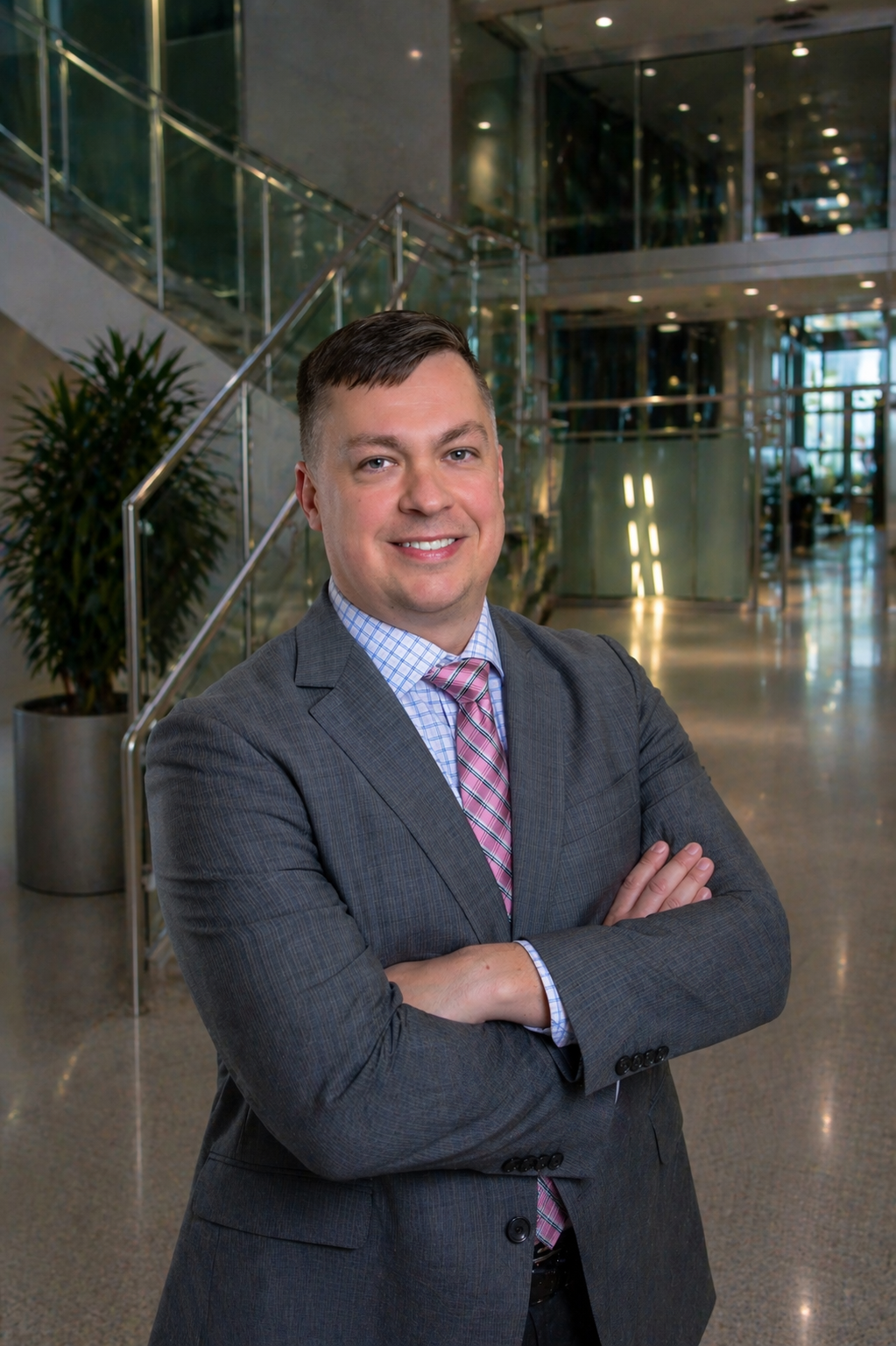 A smiling man in a gray suit stands with arms crossed in a modern office lobby.