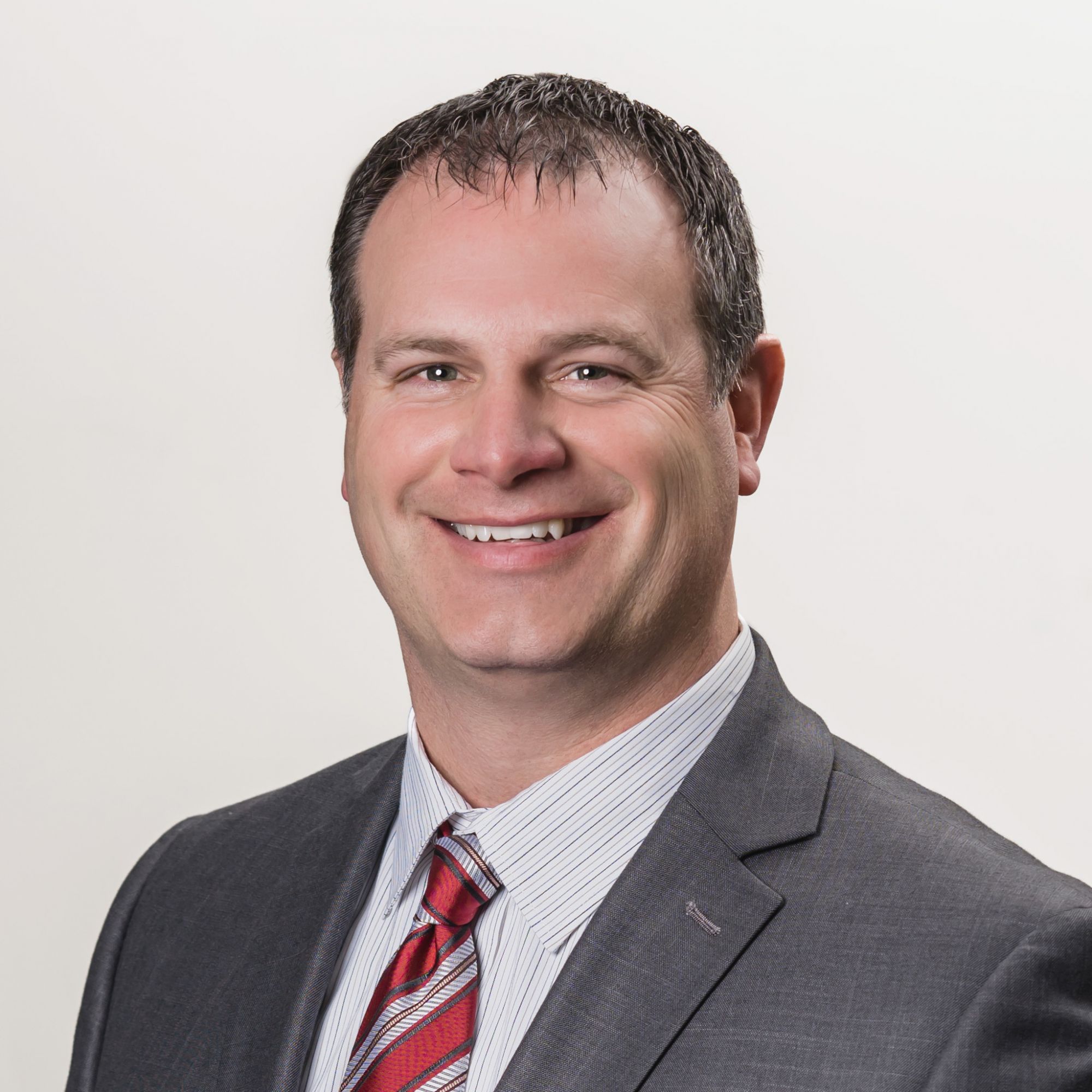 Smiling man in a suit and tie against a plain background.