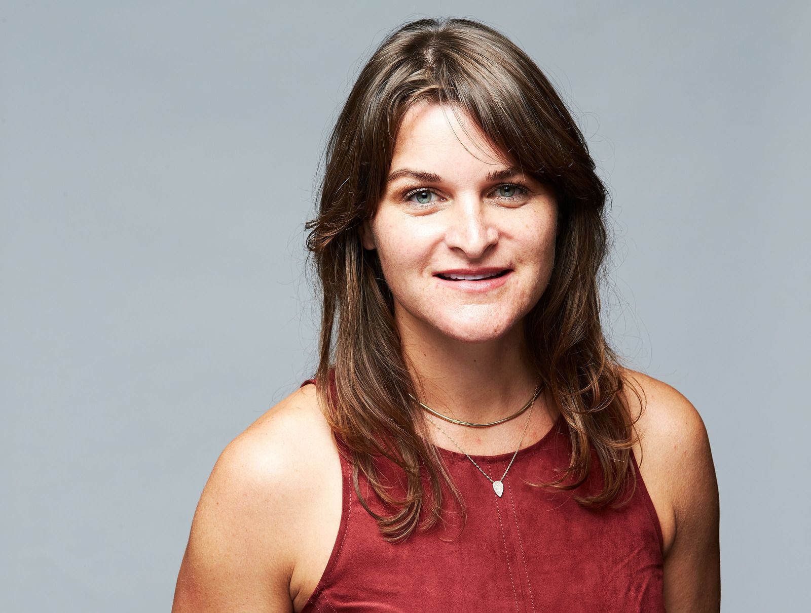 Woman with long brown hair wearing a burgundy top, smiling against a gray background.
