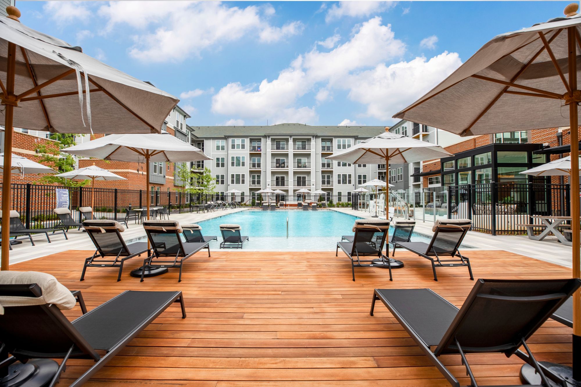 View of a pool area with lounge chairs and umbrellas in an apartment complex.