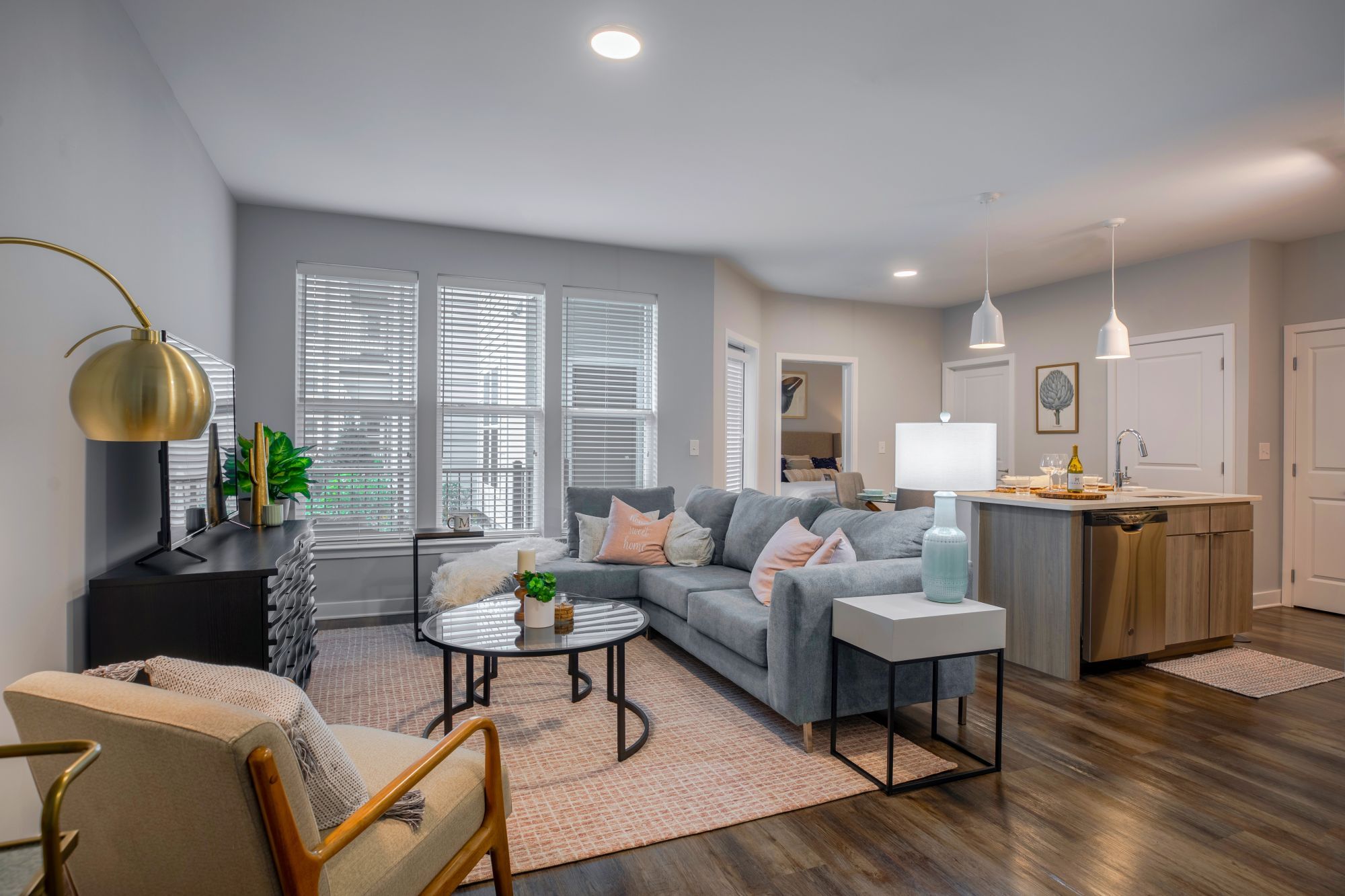 Modern living room with a gray sofa, coffee table, and kitchen area in a bright, airy space.