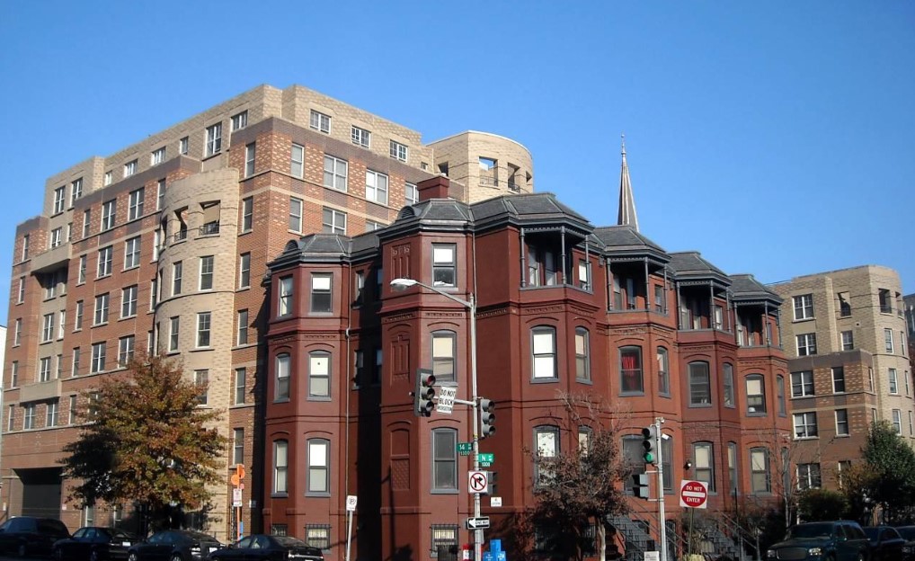 Historic rowhouse-style residential building with a red brick facade and decorative bay windows located at a city street corner.