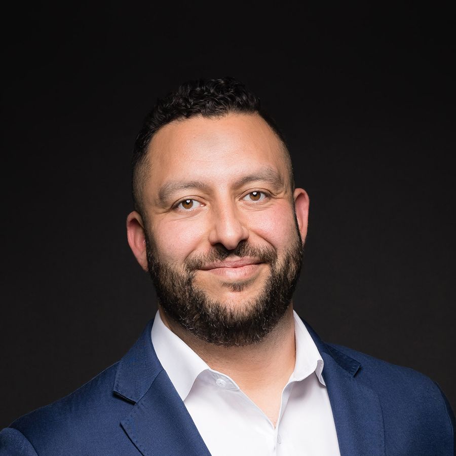 Smiling man in a suit against a dark background.