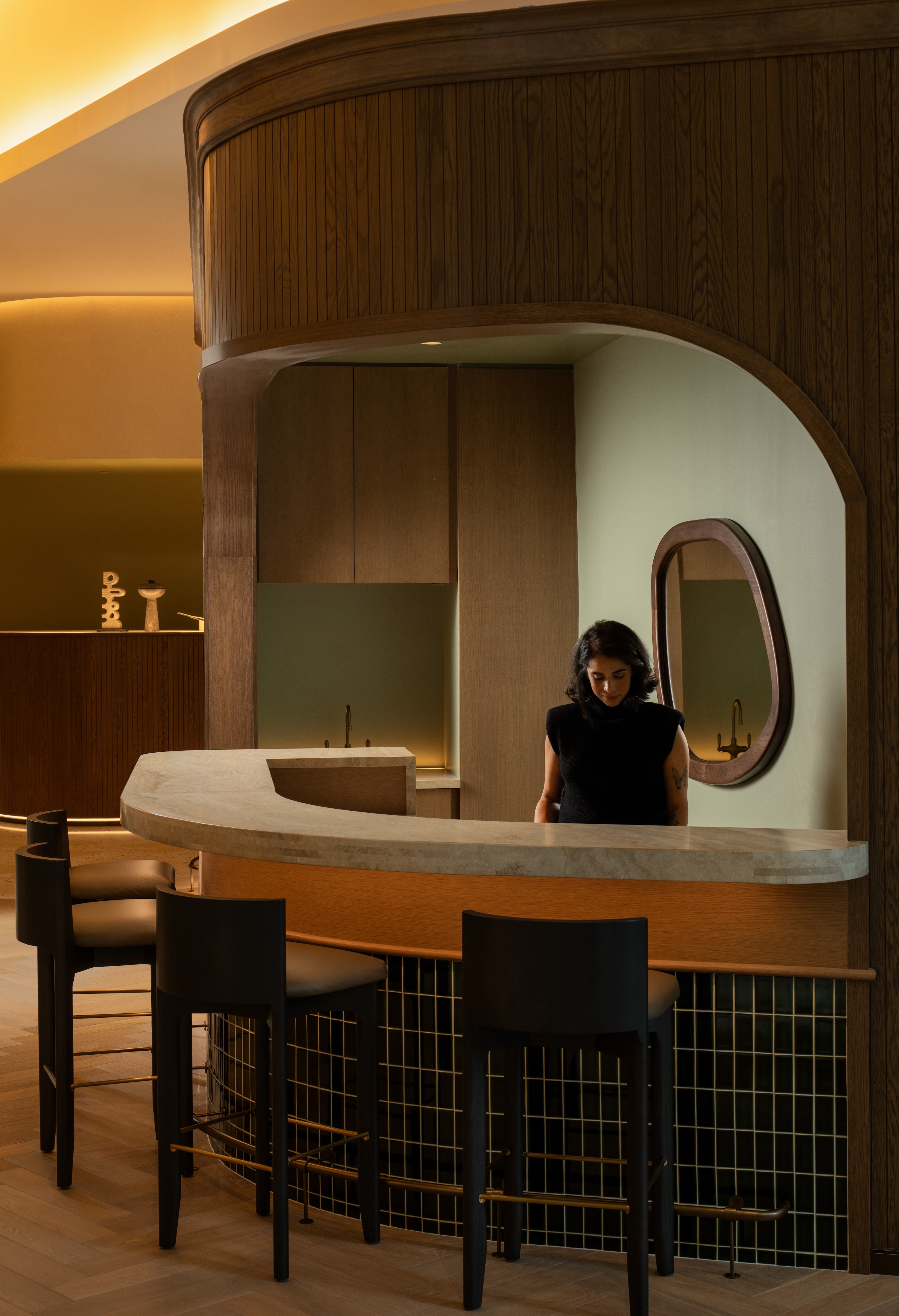A woman stands behind a modern, curved reception desk in an elegant interior.