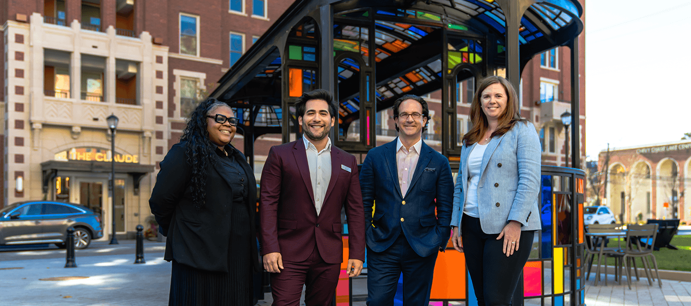 Four people stand in front of a colorful shelter in an urban setting.