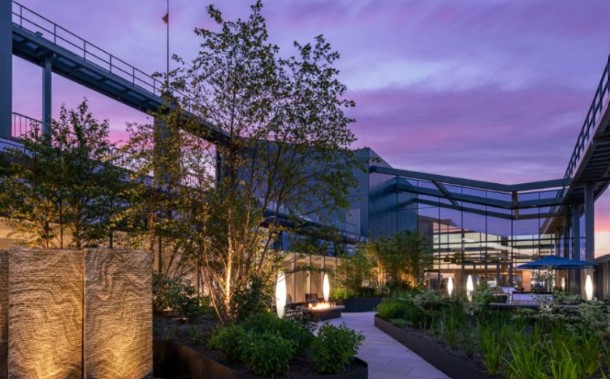 Landscaped outdoor courtyard at a modern residential building during dusk, featuring walking paths, decorative lighting, seating areas, and lush plantings.