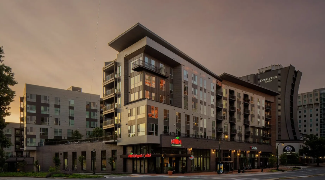 Modern multi-story apartment building at dusk, with retail space below.