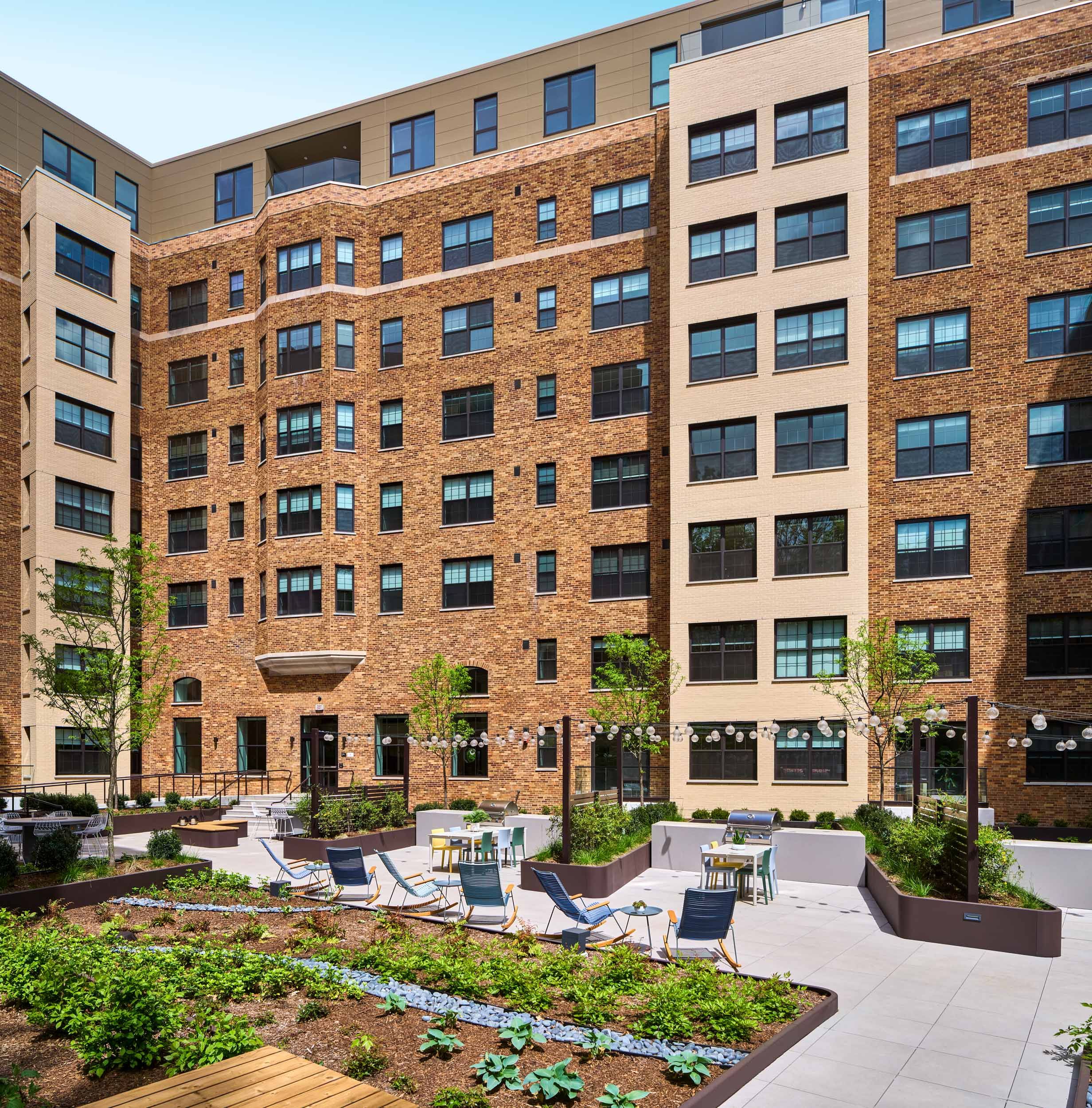 Modern brick apartment building with a landscaped courtyard and seating areas.