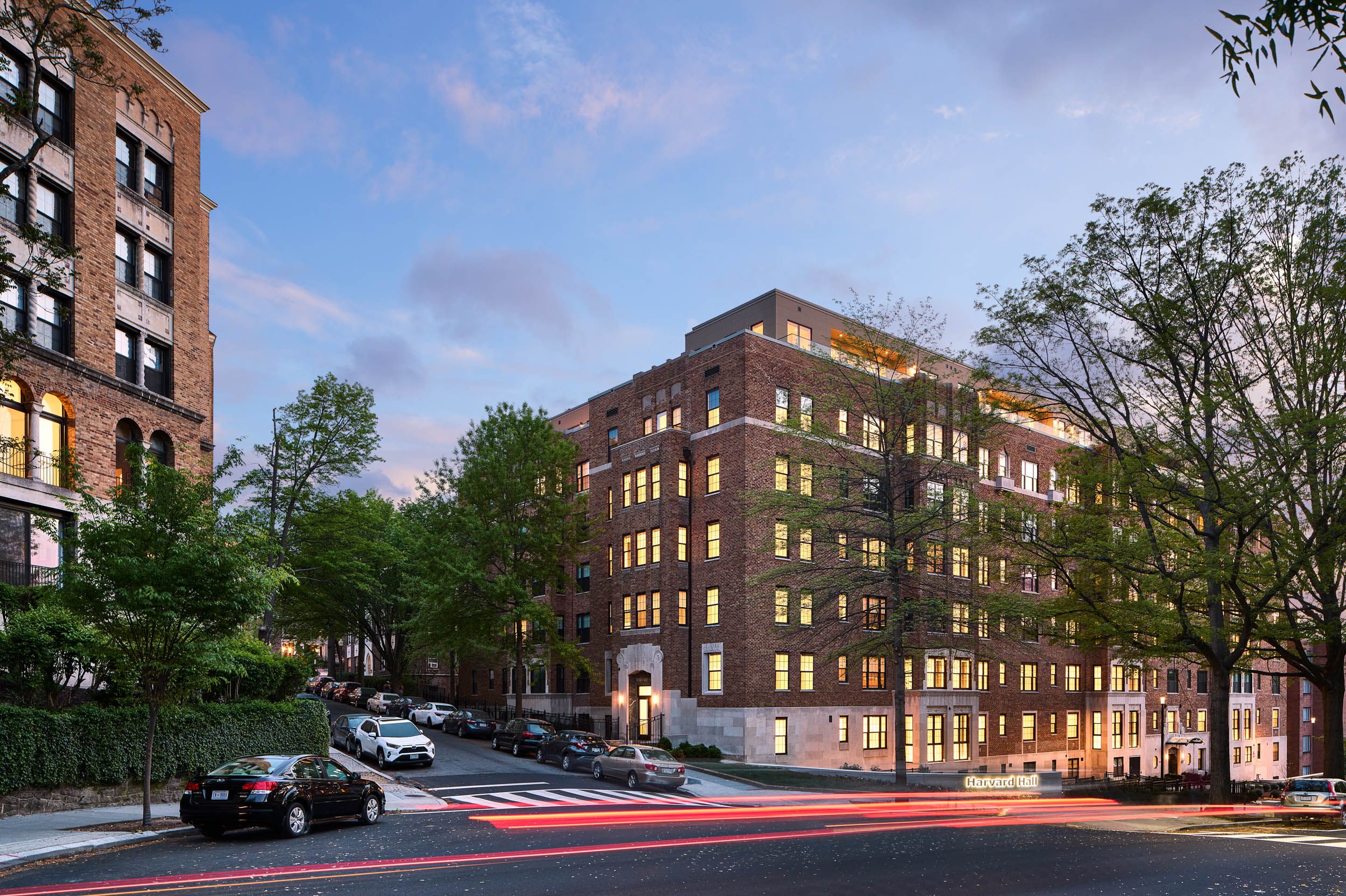 A modern apartment building on a sloped street with trees and evening sky.