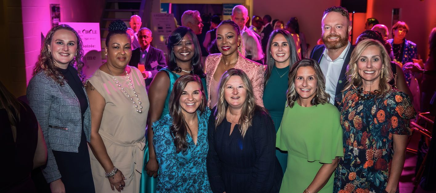 A diverse group of ten people posing together at a lively event with colorful lighting.