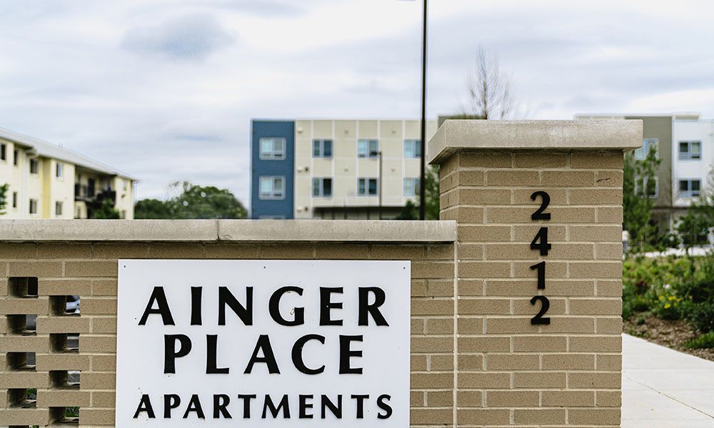 Sign for Ainger Place Apartments with a modern building in the background.