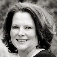 Woman with shoulder-length brown hair smiling in a black and white portrait.