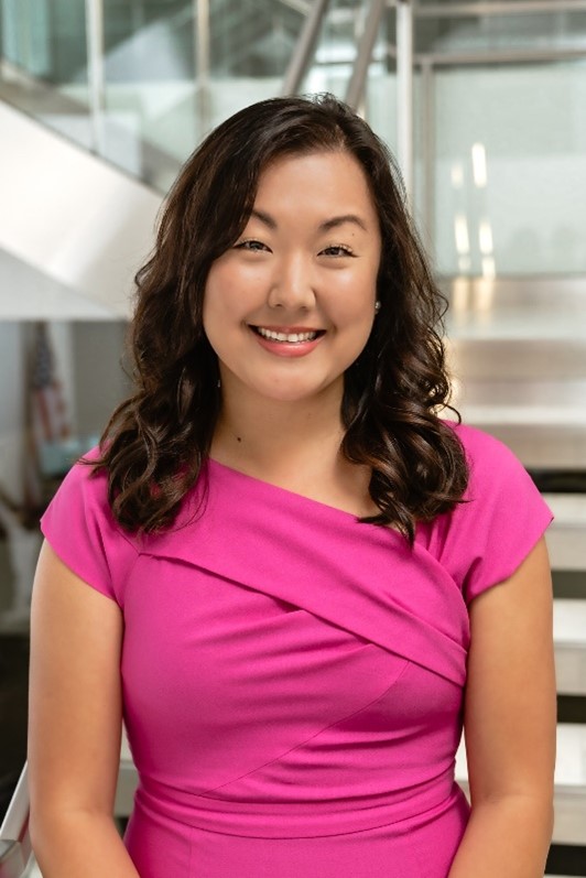 Portrait of Annie Wildasin smiling, wearing a pink dress in a modern indoor setting.
