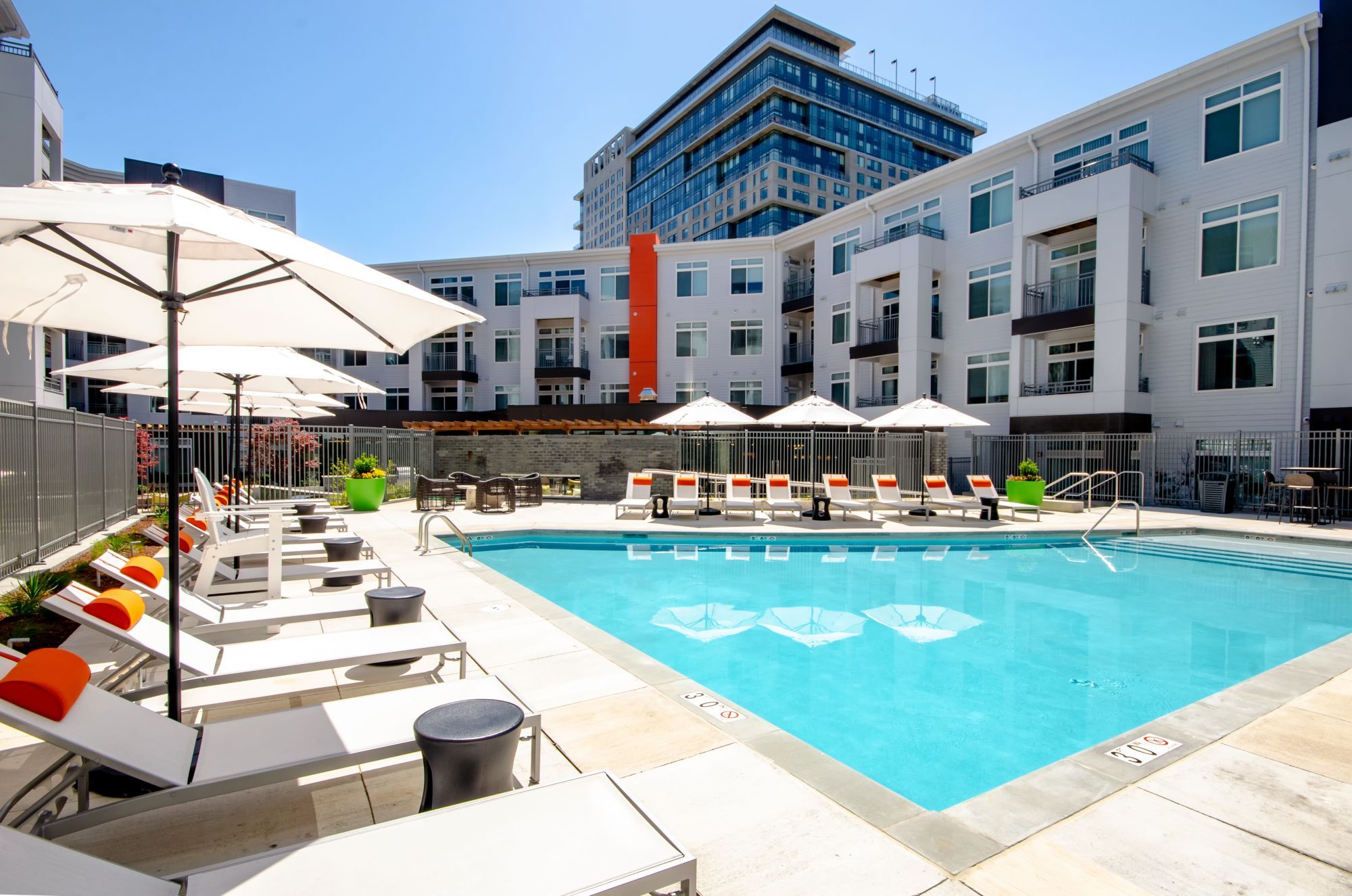 Modern apartment complex with a swimming pool and lounge chairs under umbrellas.