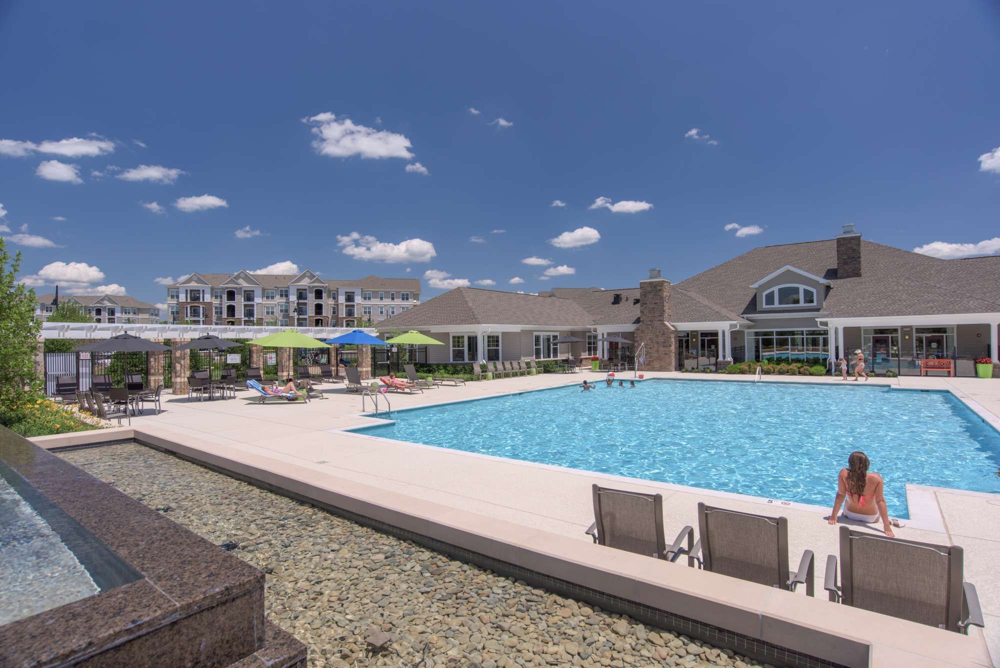 A spacious pool area with loungers and a clubhouse under a clear blue sky.