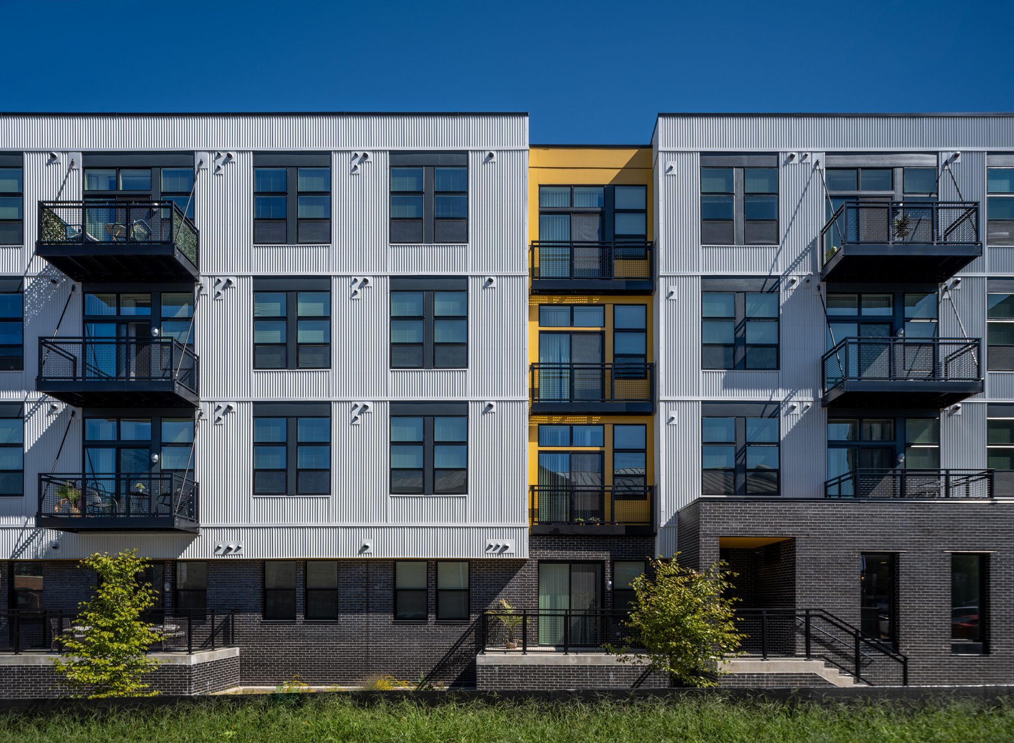 Modern apartment building with balconies and colorful accents against a clear blue sky.