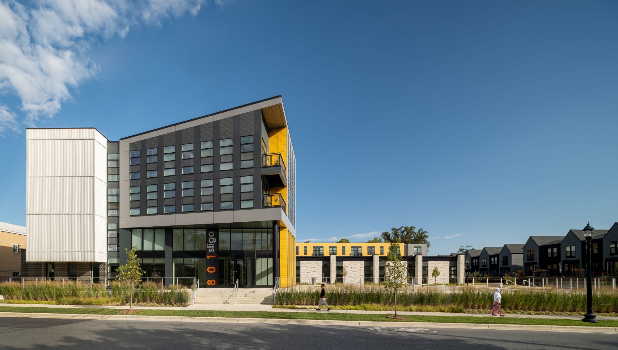 Modern multi-story building with a mix of large windows and bold colors against a clear blue sky.