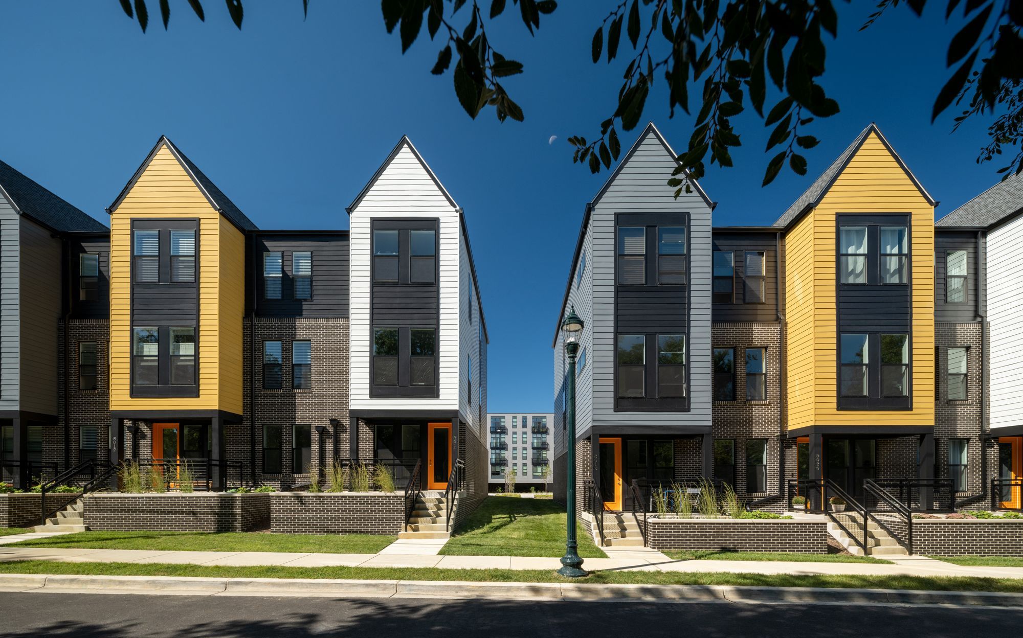 Row of modern townhouses with contrasting colors under a clear blue sky.