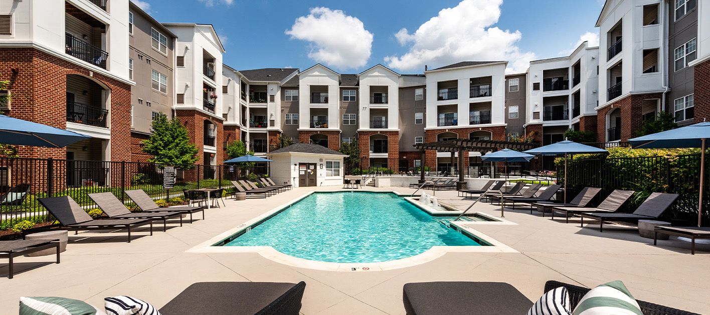 Luxurious apartment complex pool area with loungers and sunshades under a blue sky.